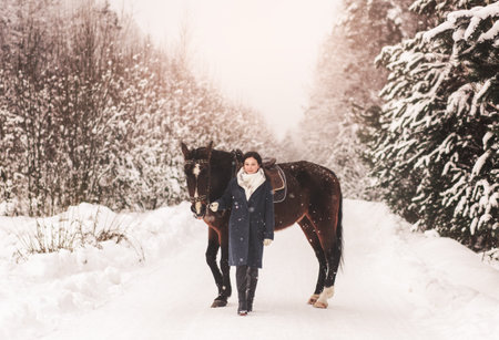 A young girl walks with a horse in the winter forestの写真素材