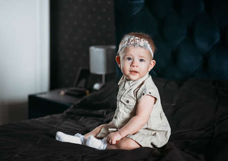 Pretty girl baby sits on a dark background. A look at the cameraの写真素材