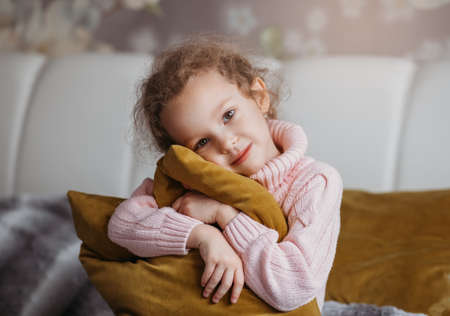 Beautiful little girl with a yellow pillow on the bed in the bedroomの写真素材