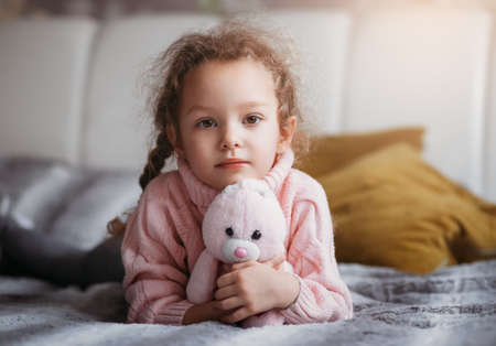 Little pretty girl with toy rabbit lies a bedの写真素材