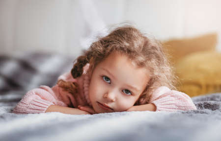 Sad little girl lies on the couch and looks at the cameraの写真素材