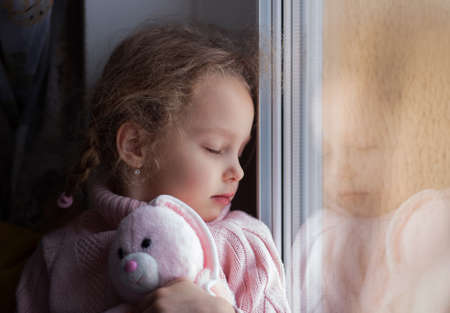 A little girl sits and looks out the window. Thoughtful