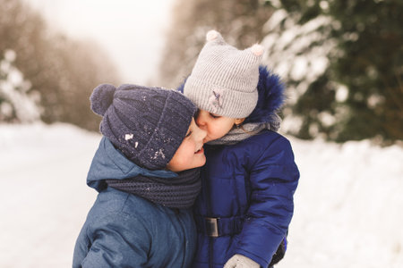 Little sister kisses her brother in nature in winterの写真素材