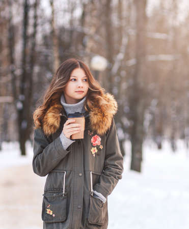 Beautiful girl enjoys snow in a winter park on a sunny day