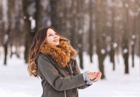 Beautiful girl enjoys snow in a winter park on a sunny dayの写真素材