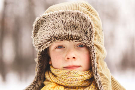 Boy with freckles in a fluffy winter hat in nature