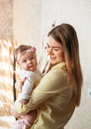 Young beautiful mother holds a little baby daughter in the room