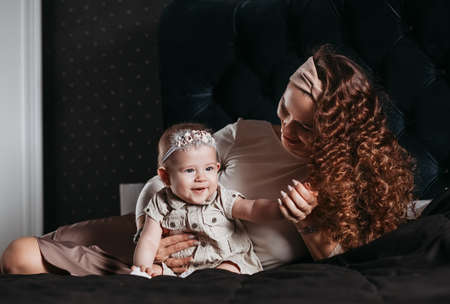 Beautiful young mother and baby daughter communicate lying on the bed on a dark backgroundの写真素材
