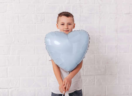 Boy holds blu heart-shaped balloon on white background