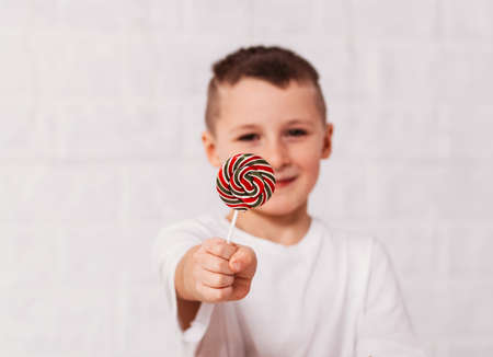 Boy holds a round multicolored lollipop on a white backgroundの写真素材