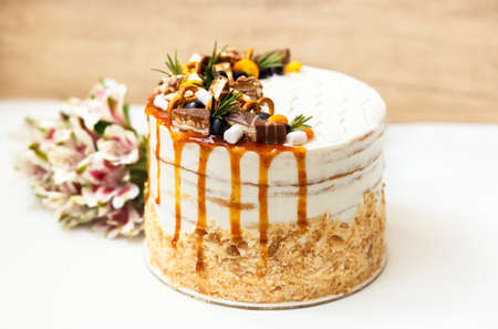 A beautiful white cake decorated with sweets, berries and fruit stands on a table with flowers