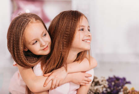 Portrait of two beautiful happy girls in a light room, cuddling and laughingの写真素材