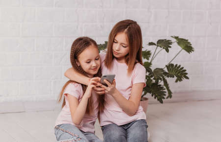 Two little schoolgirl girls look at the smartphone screenの写真素材