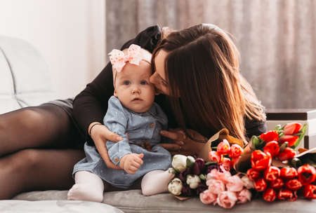 Mom kisses a baby daughter on the bed with a large bouquet of flowers tulips. Mother's dayの写真素材