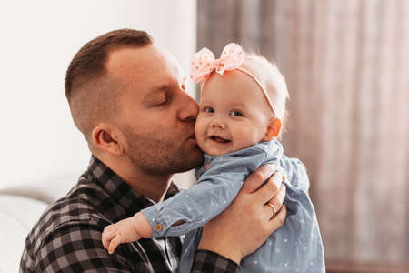 A handsome young man father kisses a little daughter. Girl infant in daddy's arms