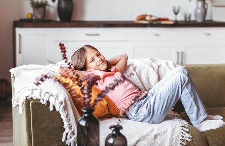 Little positive girl resting on the couch in the roomの写真素材