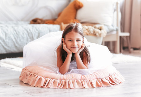 Happy little girl lies on the floor in a light bedroom. A look at the cameraの写真素材