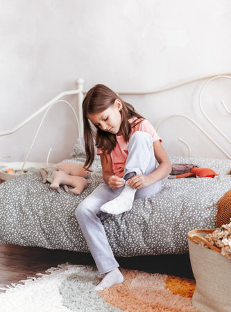 A little girl wears socks sitting on a bed in her bedroom. The kid's going to school. Independent childrenの写真素材