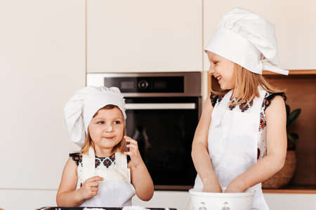 Two little happy girls in chef hats play with flour in the kitchenの写真素材