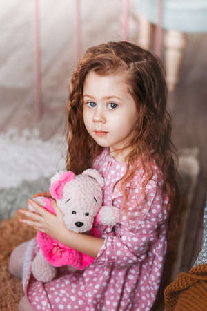A beautiful little girl hugs a soft toy bear in a light room.の写真素材