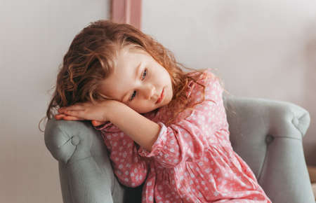 Portrait of a beautiful brooding girl in a chair. Children's dreams. Melancholy emotionsの写真素材