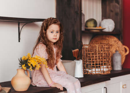 A little girl sits on the kitchen table in the kitchen. Household helpの写真素材