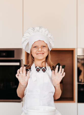 A little funny girl in a white chef hat plays with flour in the kitchen. Baby cooksの写真素材