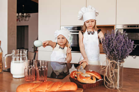 Two cute girls in chef hats and white aprons cook in the kitchen.の写真素材