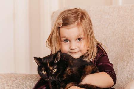 A little cute girl holds a black cat in her arms. Girl at home with her pet. Little girl loves her cute kitten.の写真素材