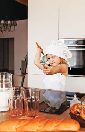 A little girl in a chef's hat plays with kitchen appliances in the kitchen