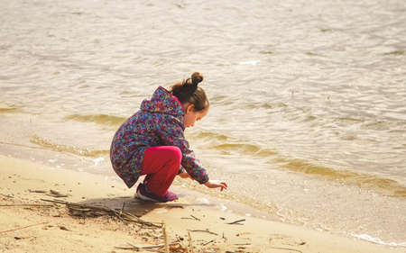 A little girl plays with water on the shore of the lakeの写真素材
