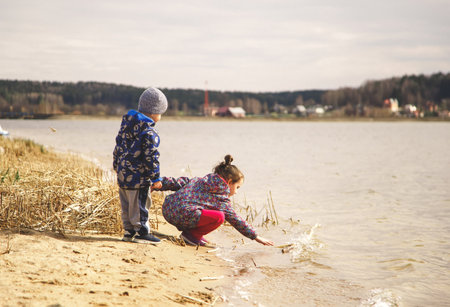 Young children play near the lake. A boy and a girl look at the water in the river. Children's friendship.の写真素材