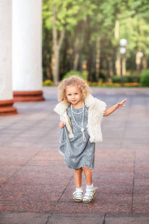 Little fashion beautiful girl poses for the camera in a shiny dress in natureの写真素材
