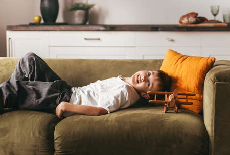 A boy lies on a sofa with a toy plane and dreams. Children's home time concept image.