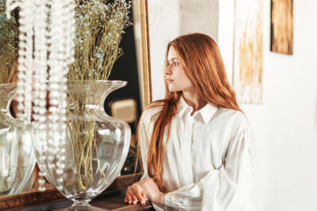 Young beautiful girl with long hair stands near the mirror in the morning in the bedroomの写真素材
