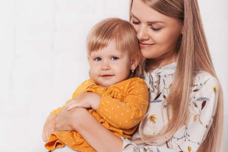 A young happy mother hugs her baby daughter against a bright background. Mother-child communication....
