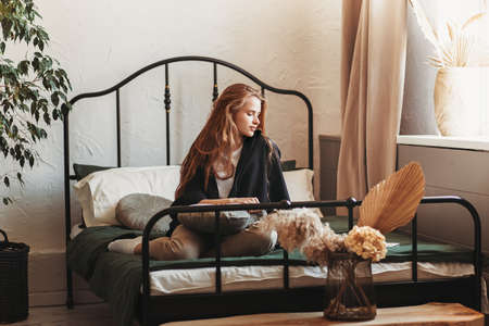 A young beautiful girl with long hair on a bed. Woman enjoying morning awakening. The concept of home coziness and comfort.の写真素材