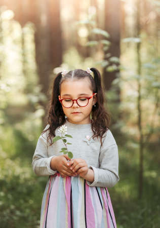 A little pretty girl holds a flower on a walk in the park in the summer on a sunny dayの写真素材