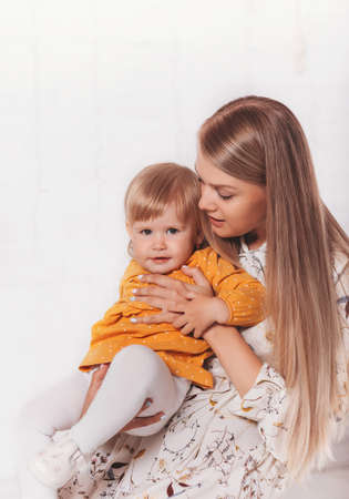 Young beautiful blonde woman is holding a little daughter on her lap. vertical