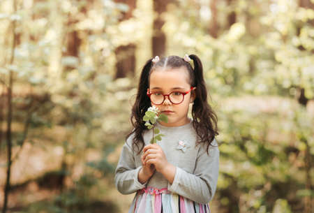 A little pretty girl holds a flower on a walk in the park in the summer on a sunny day