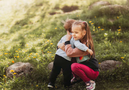 Older sister hugs her little brother in summer in the parkの写真素材