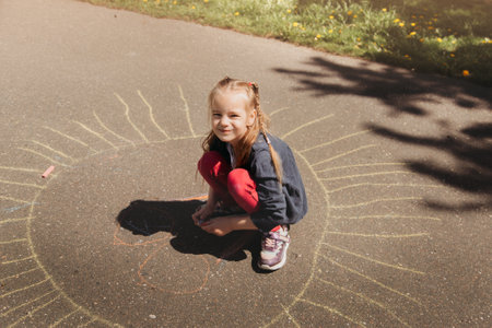 Girl preschooler draws with chalk on the asphalt in summer in the parkの写真素材