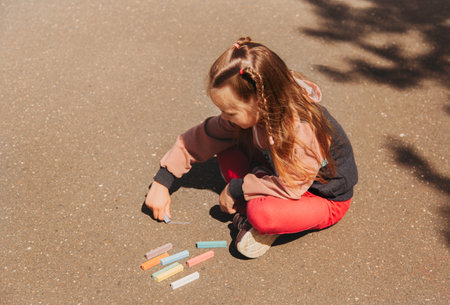 Girl preschooler draws with chalk on the asphalt in summer in the parkの写真素材