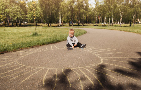 Little boy Todler draws chalk on the asphalt, in the summer in the park