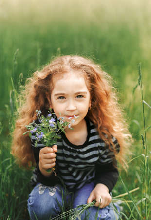 Little girl with curly hair in the park with a bouquet of wildflowersの写真素材