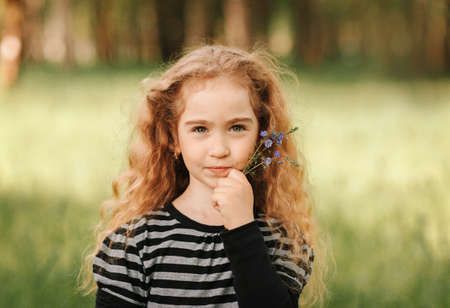 Little girl with curly hair in the park with a bouquet of wildflowersの写真素材