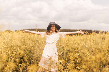 A young happy girl enjoys nature on the field of blossoming canola. The corcept of youth and freedom