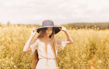 Portrait of a beautiful young girl with long hair against the background of rapeseed flowers. Youth and natureの写真素材