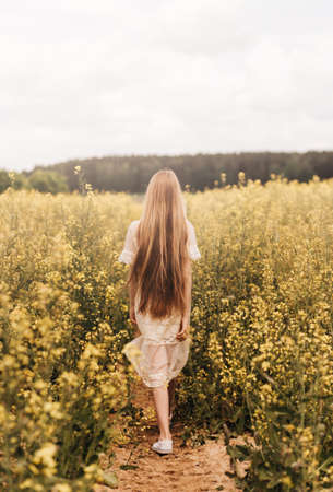 Portrait of a beautiful young girl in a hat against the background of a rapeseed field.の写真素材
