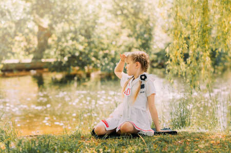 A girl with two pigtails sits on the grass in the summer near the river. Concept of happy childhood and summer leisure.の写真素材